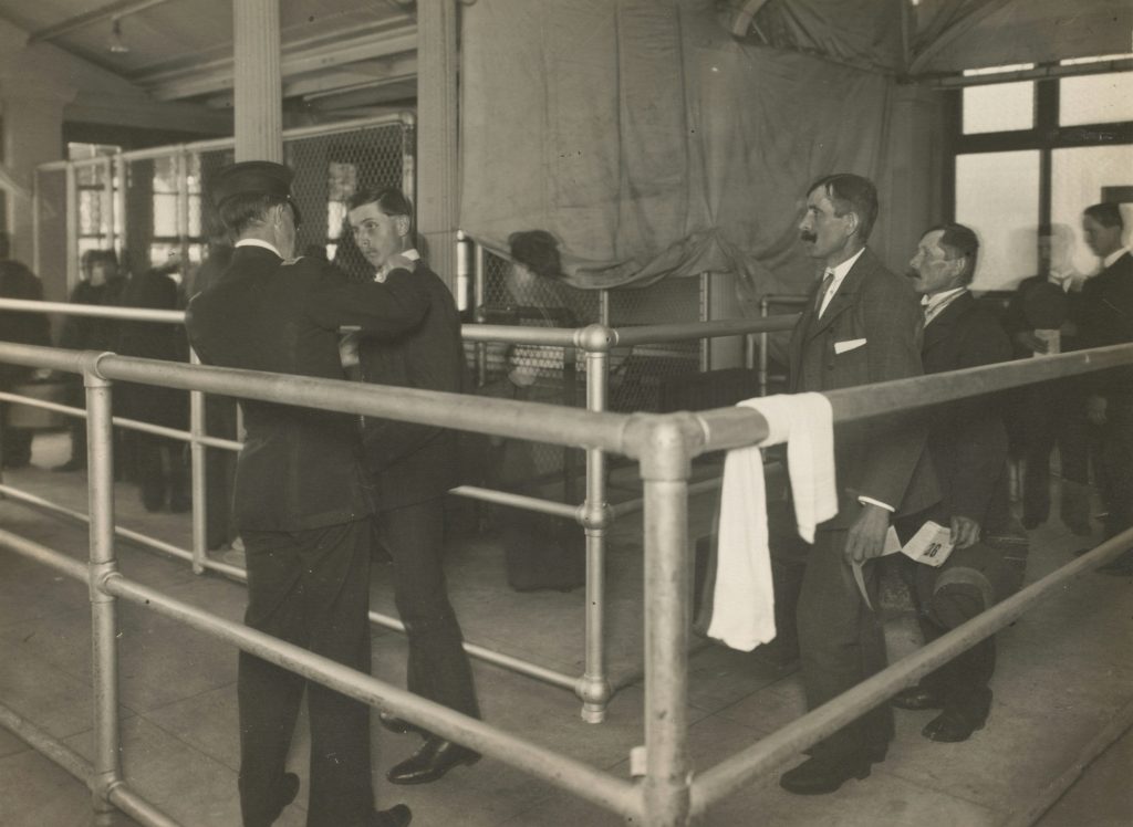 Greyscale image of men being medically inspected at Ellis Island